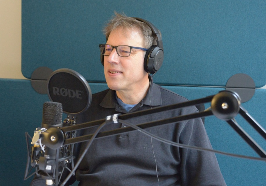 Stefan Bach, DIW-Steuerexperte; Das Bild zeigt Stefan Bach, wissenschaftlicher Mitarbeiter der Abteilung Staat und Steuerexperte des DIW Berlin, der in einem Aufnahmestudio sitzt und sich auf eine Aufnahme vorbereitet. Die Person trägt Kopfhörer und spricht in ein Mikrofon.<br />
Visuelle Elemente:<br />
Person:<br />
Die Person trägt eine Brille und Kopfhörer.<br />
Sie ist in ein dunkles Hemd oder eine Bluse gekleidet.<br />
Mikrofon:<br />
Vor der Person befindet sich ein Mikrofon der Marke "RØDE".<br />
Das Mikrofon ist auf einem Ständer montiert und auf die Person ausgerichtet.<br />
Hintergrund:<br />
Der Hintergrund besteht aus einer blauen Wand, die typisch für ein Aufnahmestudio ist.<br />
Es gibt auch ein Mikrofonarm, der das Mikrofon hält.<br />
Zusätzliche Informationen:<br />
Das Bild vermittelt den Eindruck einer professionellen Aufnahmeumgebung, möglicherweise für Podcasts, Sprachaufnahmen oder Interviews.<br />
Die Person scheint sich auf eine Aufnahme oder ein Gespräch vorzubereiten.<br />
Diese Beschreibung bietet einen Überblick über die Szene einer Person, die sich in einem professionellen Aufnahmeumfeld befindet.